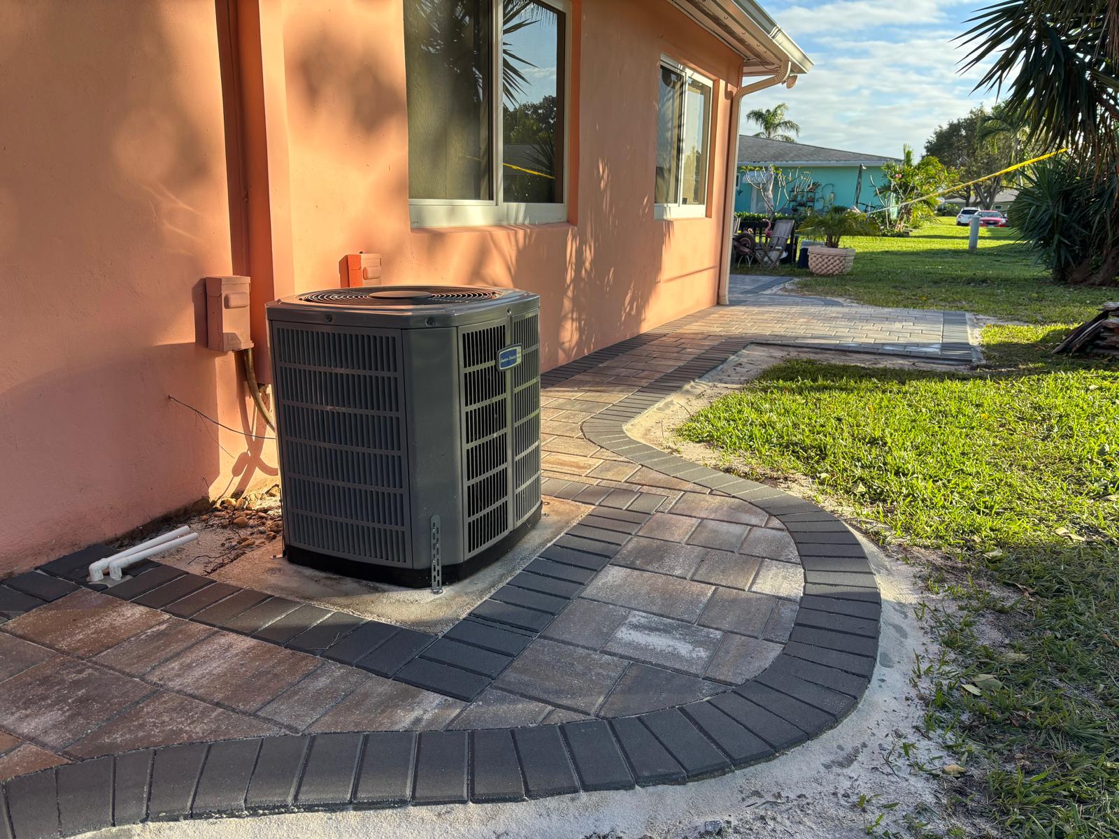 Grey paver walkway curving around an AC unit and home corner